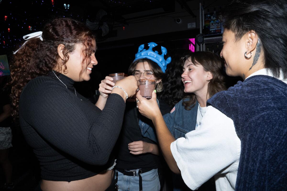 Four people stand in a group, smiling and holding up beverages.