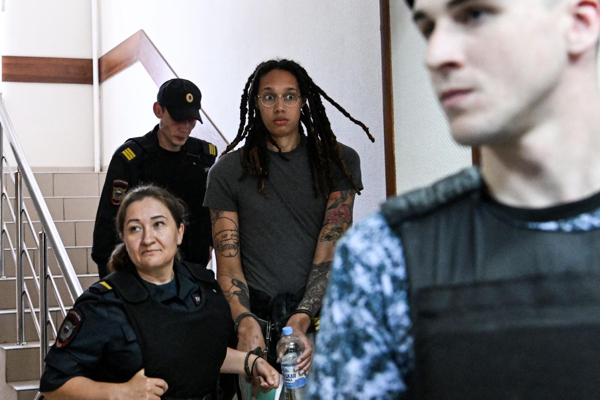 Griner, wide-eyed, in a stairwell, escorted by people in uniform.