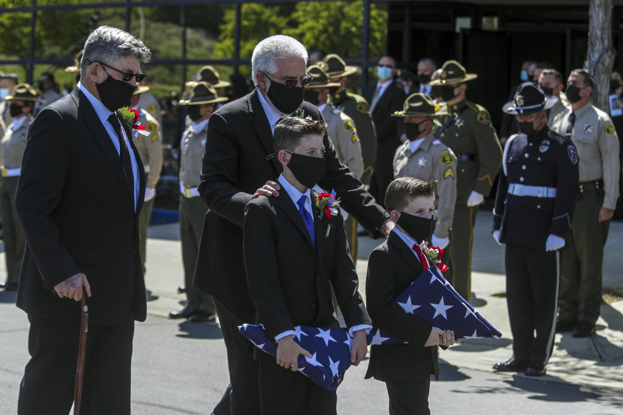 Two boys in suits and masks walk while carrying folded American flags.
