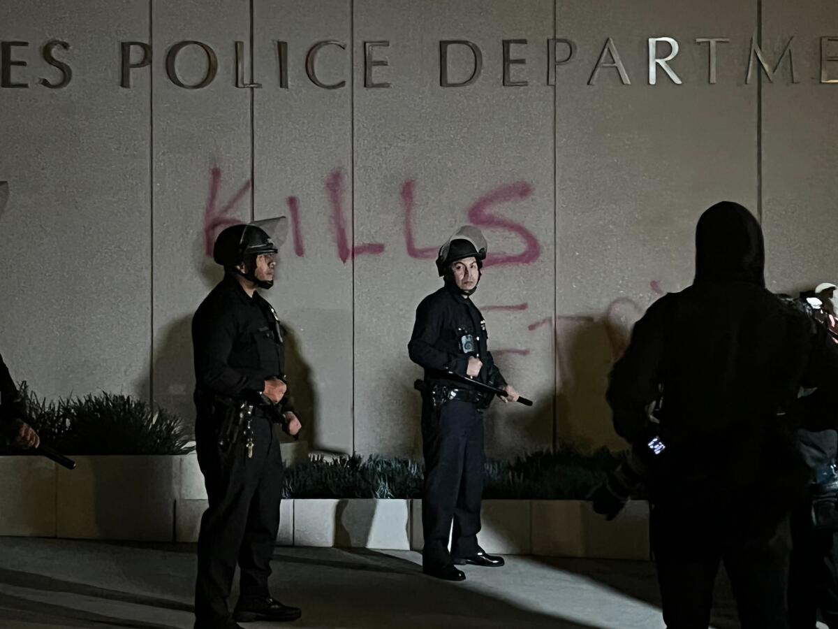 Police officers in front of the word "kills" spray painted underneath the "Los Angeles Police Department" sign