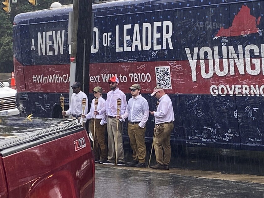 In this image provided by NBC29, five people holding tiki torches stand in the rain by the campaign bus for GOP gubernatorial candidate Glenn Youngkin, outside the Guadalajara Mexican Restaurant on Market Street in Charlottesville, Va., Friday, Oct. 29, 2021. The anti-Donald Trump group The Lincoln Project is taking credit for the group of five people who showed up at a Charlottesville campaign stop by Youngkin. The appearance recalled the torch-bearing white supremacists who descended on the city during two days of violence in 2017. (Elizabeth Holmes/NBC29 via AP)