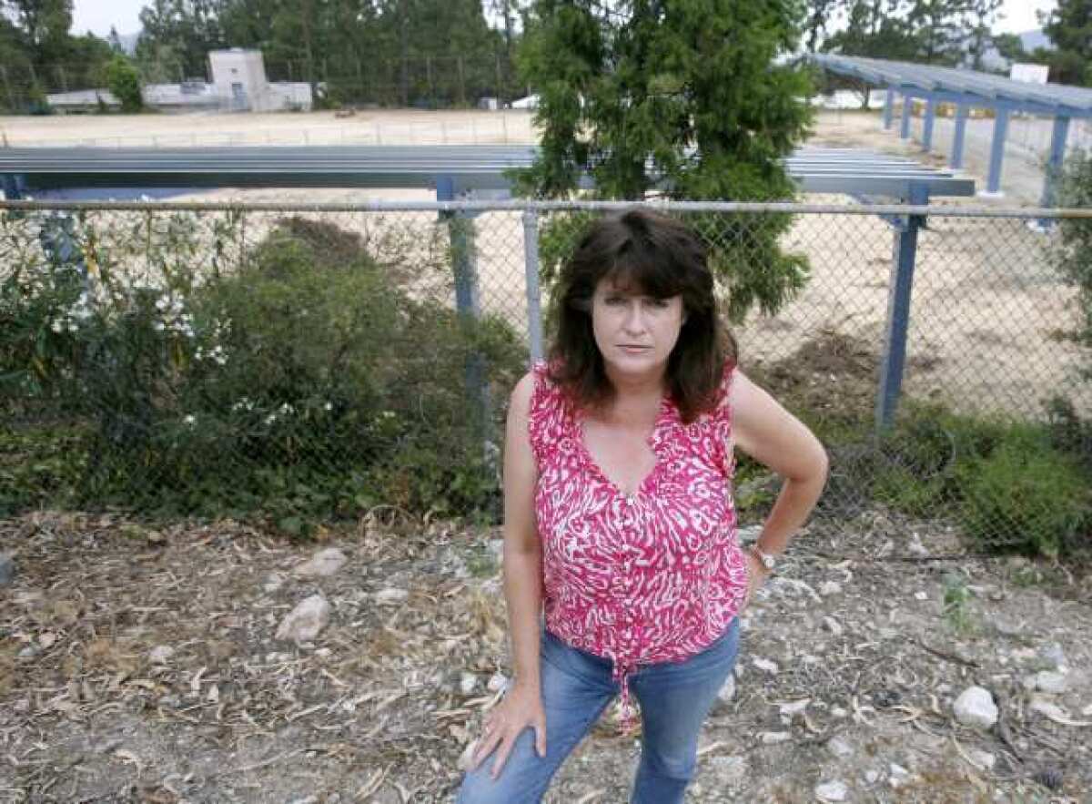 Melody McCormick stands in her neighbor's yard at 2320 El Moreno St. where a good look at the solar panel structure being erected can be seen on the campus of Mountain Avenue Elementary School in La Crescenta.
