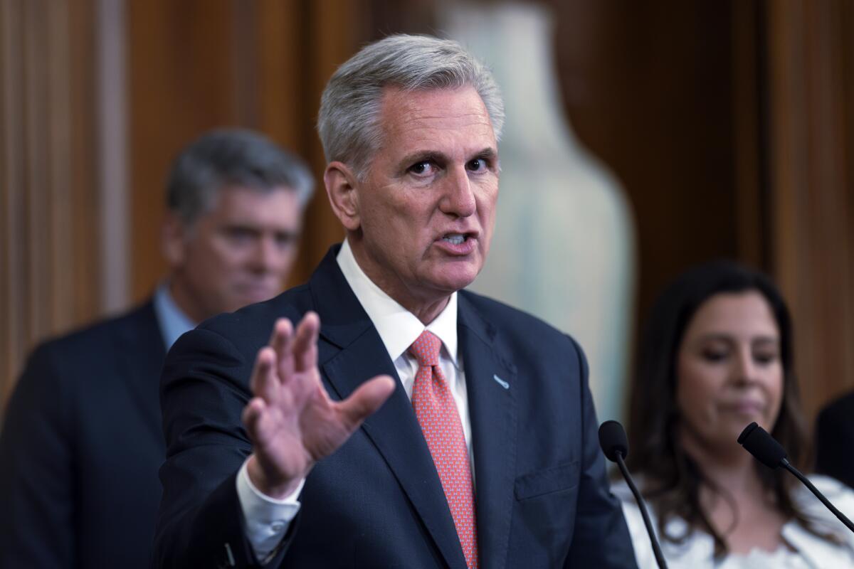 Kevin McCarthy holds up his hand while speaking, with a man and woman in the background.
