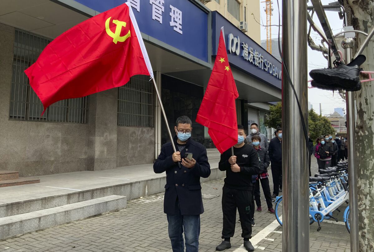 Residents carry the Communist Party flag and the Chinese national flag as others prepare to take part in the first round of mass COVID tests in the Jingan district of western Shanghai, China, Friday, April 1, 2022. As residents of western Shanghai start a four day lockdown for mass testing, some in eastern Shanghai about to end their lock down are being told they will be confined to their homes for at least 10 more days. It was the latest wrinkle in the lockdown of China's largest city as it struggles to eliminate an omicron-driven coronavirus outbreak under China's zero-COVID policy. (AP Photo/Chen Si)