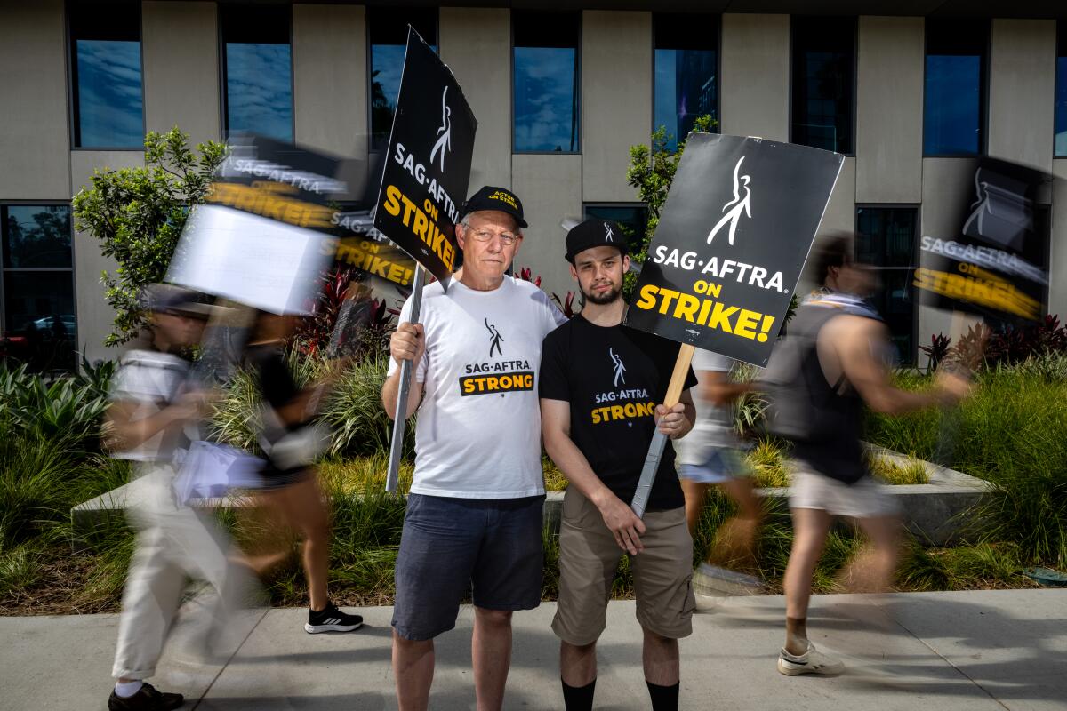 Two men wearing caps hold SAG-AFTRA signs.