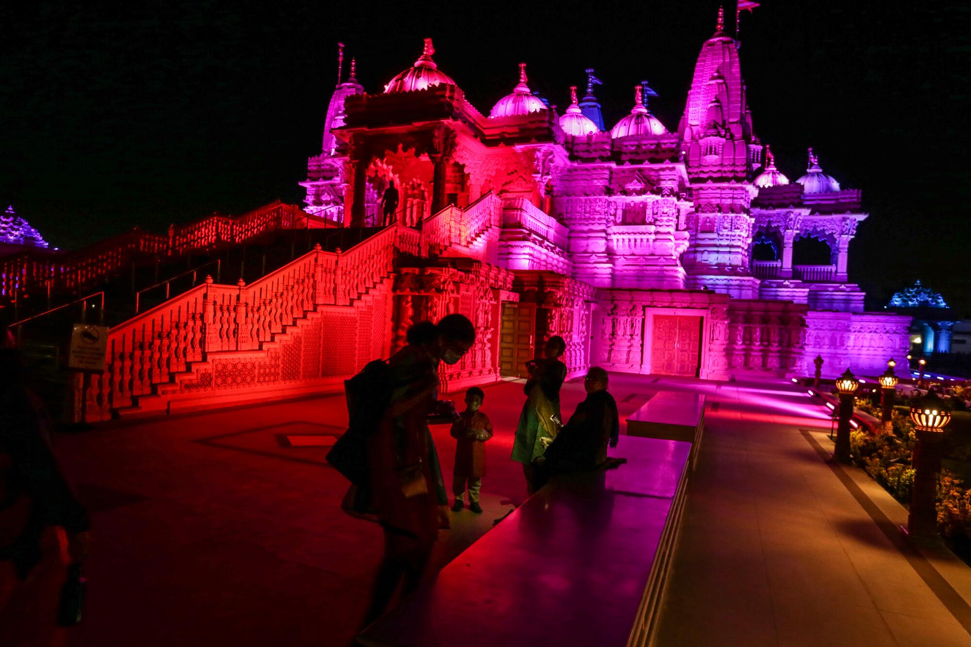 A family outside a Hindu temple bathed in red, purple and blue light