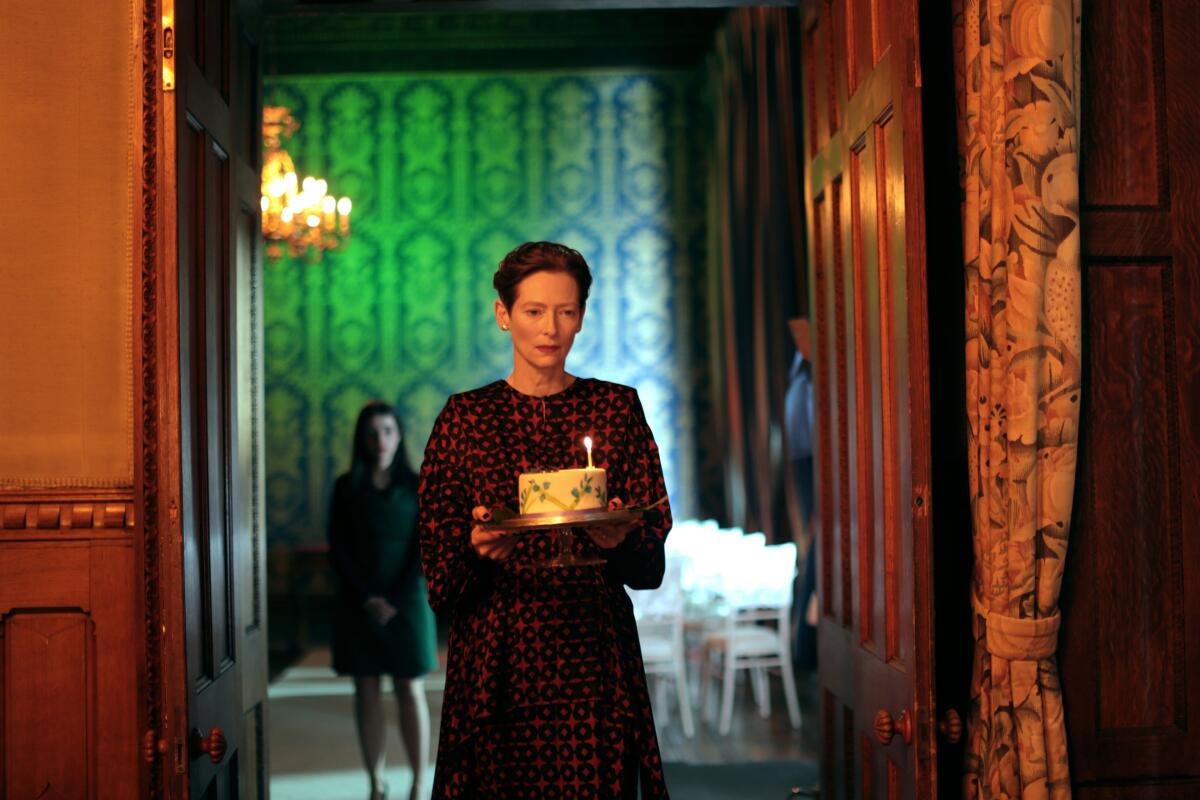 A woman carries a cake with a single candle into a room 