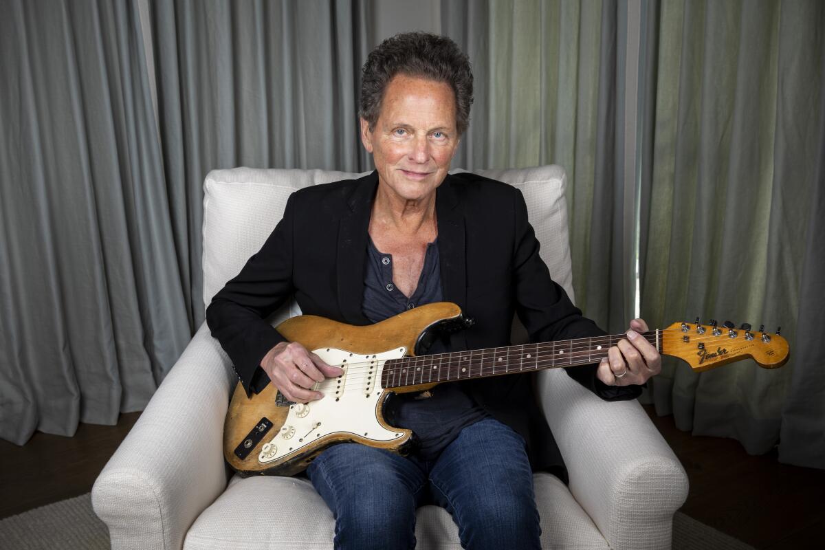 Lindsey Buckingham sitting in a chair holding a guitar