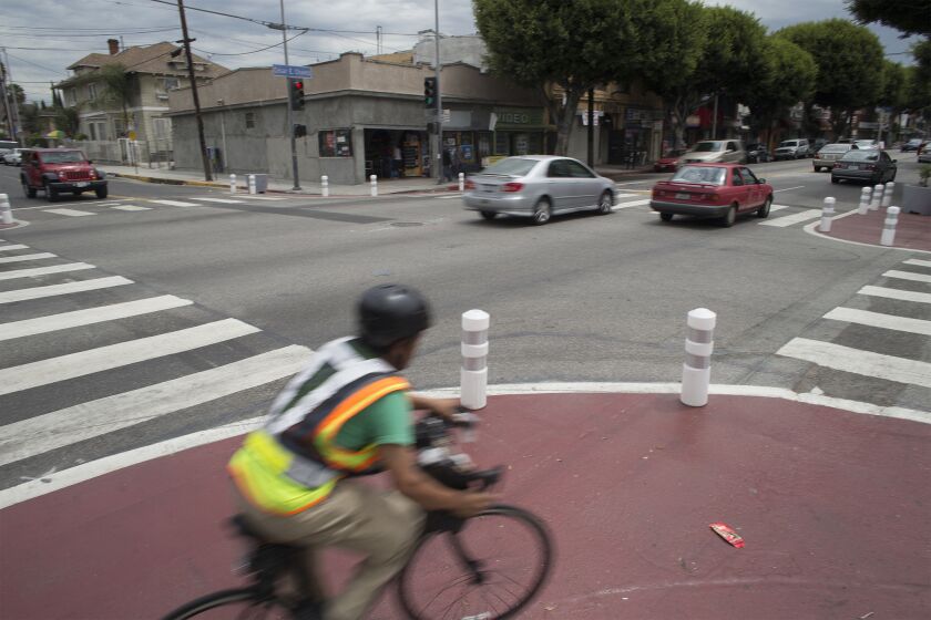A cyclist rounds the corner where the curbs have been extended and white pylons mark areas designated with red paint to help slow traffic at the intersection of Cesar Chavez Boulevard and St. Louis Street in Los Angeles.