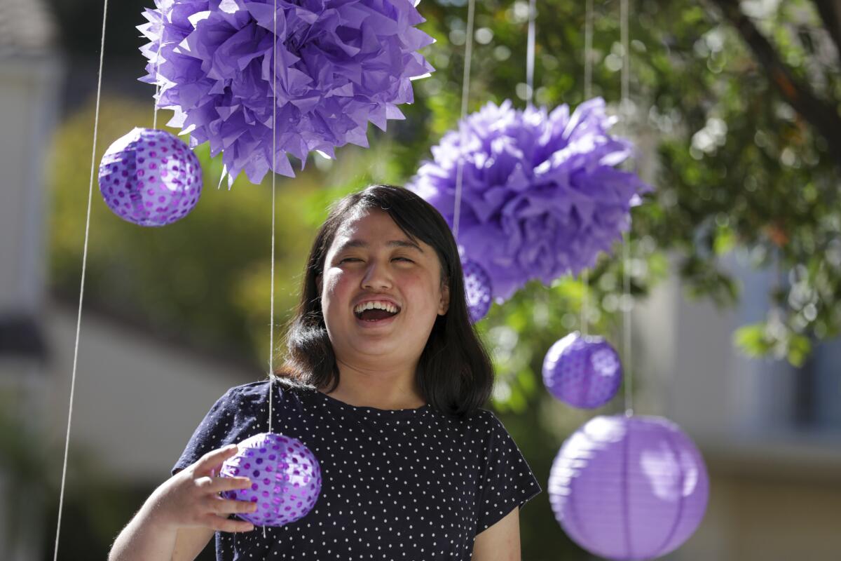 A girl laughs as she stands surrounded by purple paper lanterns and decorations