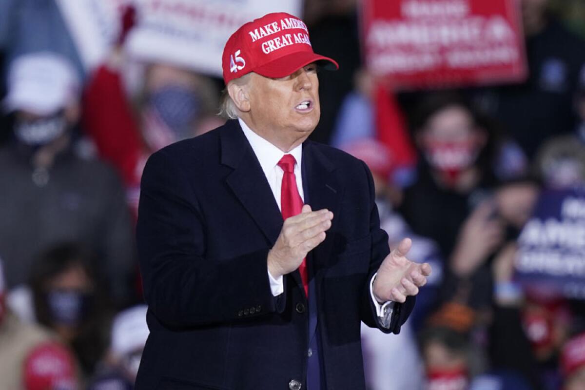 Donald Trump, in a MAGA hat, claps his hands.