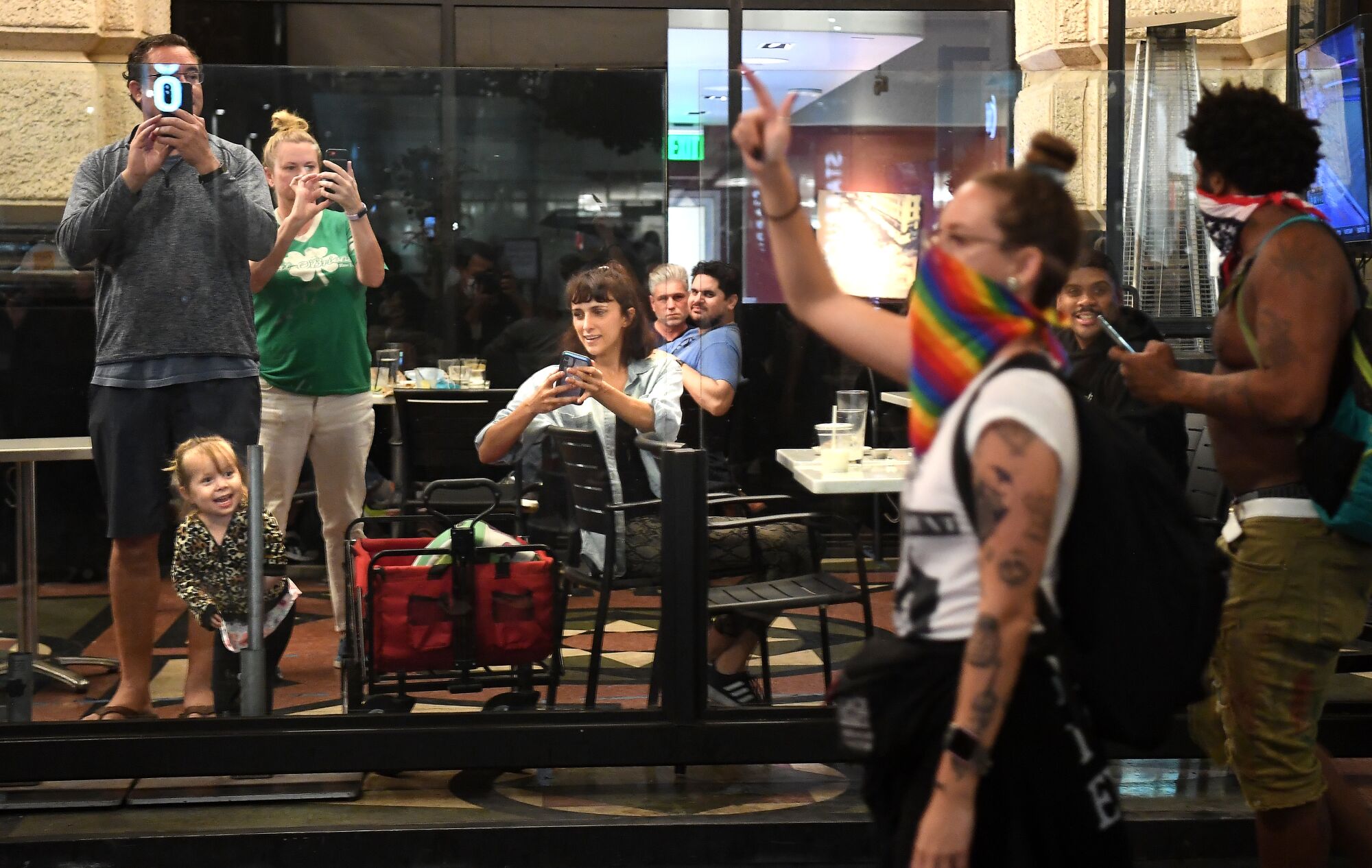 Protesters walk along 7th St. as diners take pictures from a restaurant in downtown Los Angeles