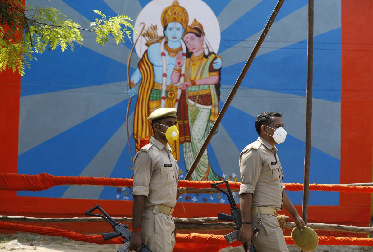 Policemen walk past an image of Hindu god Ram on the eve of a groundbreaking ceremony of a temple dedicated to Ram in Ayodhya, India, Tuesday, Aug. 4, 2020. Wednesday's groundbreaking ceremony follows a ruling by India's Supreme Court last November favoring the building of a Hindu temple on the disputed site in Uttar Pradesh state. Hindus believe their god Ram was born at the site and claim that the Muslim Emperor Babur built a mosque on top of a temple there. The 16th century Babri Masjid mosque was destroyed by Hindu hard-liners in December 1992, sparking massive Hindu-Muslim violence that left some 2,000 people dead. (AP Photo/Rajesh Kumar Singh)