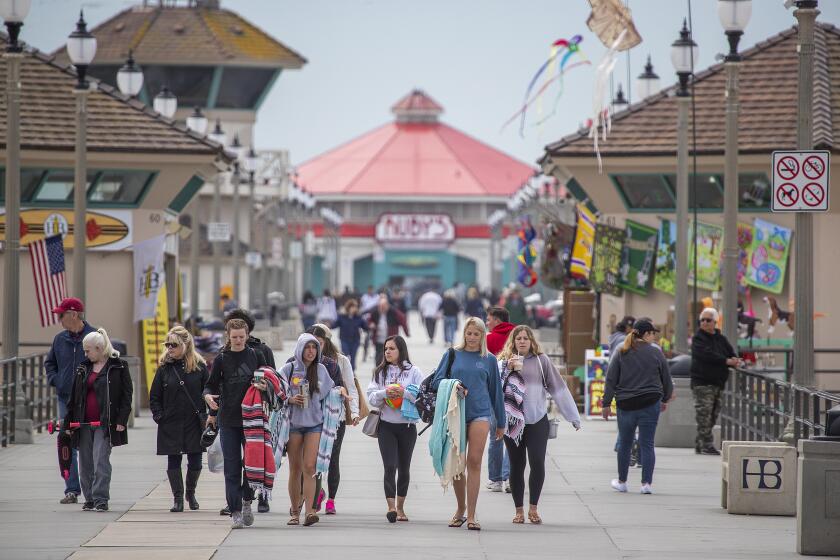 HUNTINGTON BEACH, CALIF. -- WEDNESDAY, MARCH 18, 2020: Spring breakers, visitors and locals walk on the pier amid coronavirus pandemic restrictions downtown Huntington Beach, Calif., on March 18, 2020. Orange County bars, breweries and wineries were ordered to close, restaurants were told to offer take-out or delivery only, and people were told not to gather to curb transmission of the coronavirus. (Allen J. Schaben / Los Angeles Times)