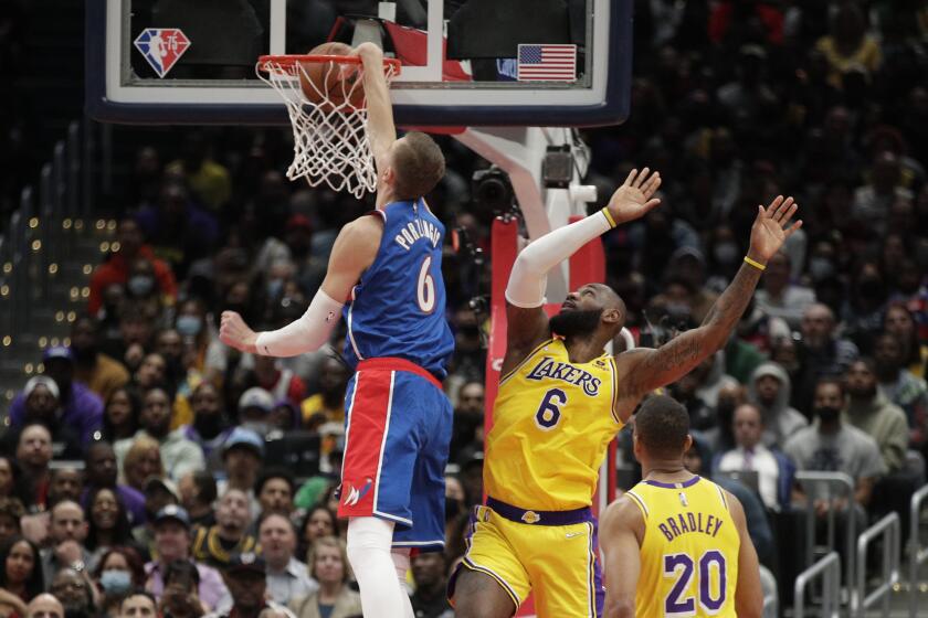 Washington Wizards' Kristaps Porzingis, left, dunks as Los Angeles Lakers' LeBron James.