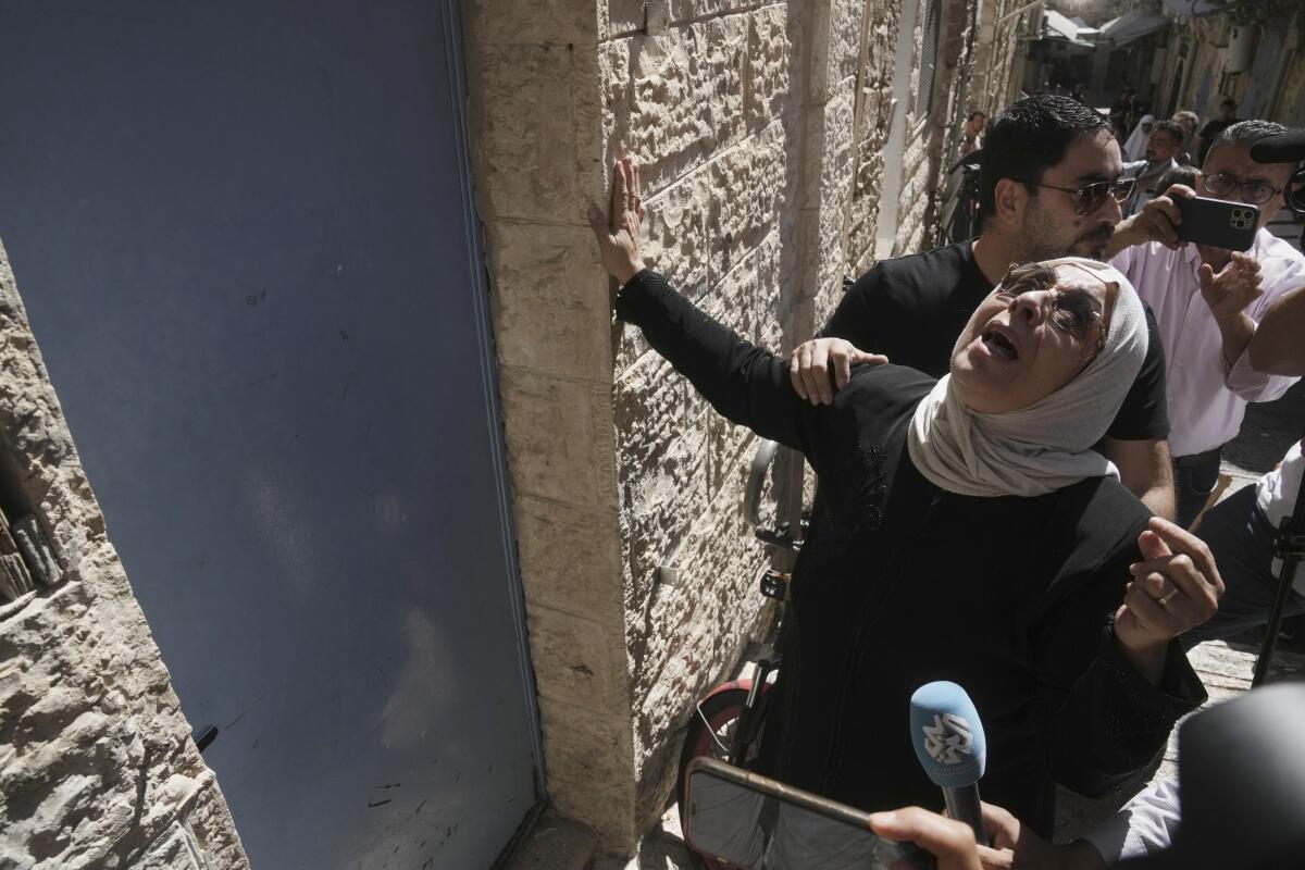 A grieving woman touches the door of a house.