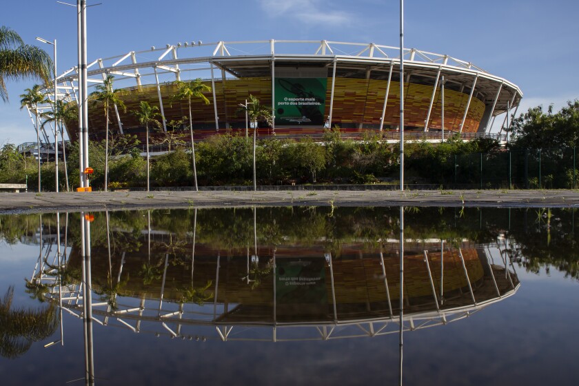 A venue at Olympic Park is reflected in a pool of water in the Barra da Tijuca western zone of Rio de Janeiro, Brazil, Thursday, June 24, 2021. With the Olympics about to kick off in Tokyo, the prior host is struggling to make good on legacy promises with Rio de Janeiro's Olympic Park venues mostly unused. (AP Photo/Bruna Prado)