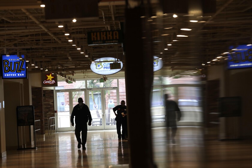 A man walks down a hallway past restaurants in a student cafeteria building