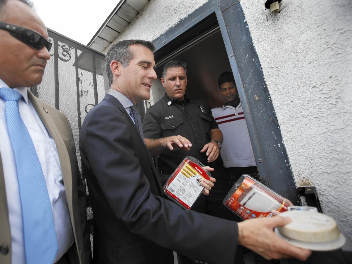 Los Angeles Mayor Eric Garcetti, center, hands off an old smoke alarm that had a worn-out battery and prepares to give two new "First Alert" smoke detectors to a resident of South L.A.