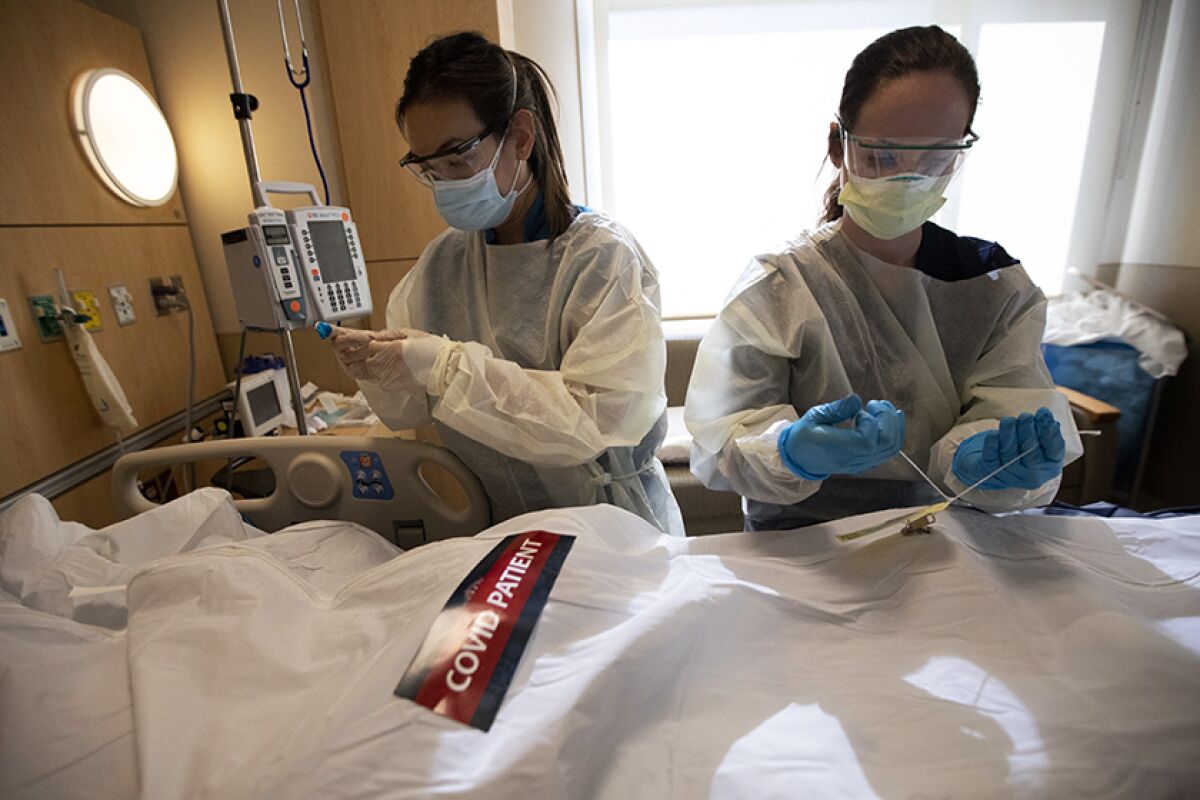 Two nurses in a hospital close a white body bag with the label "COVID patient"