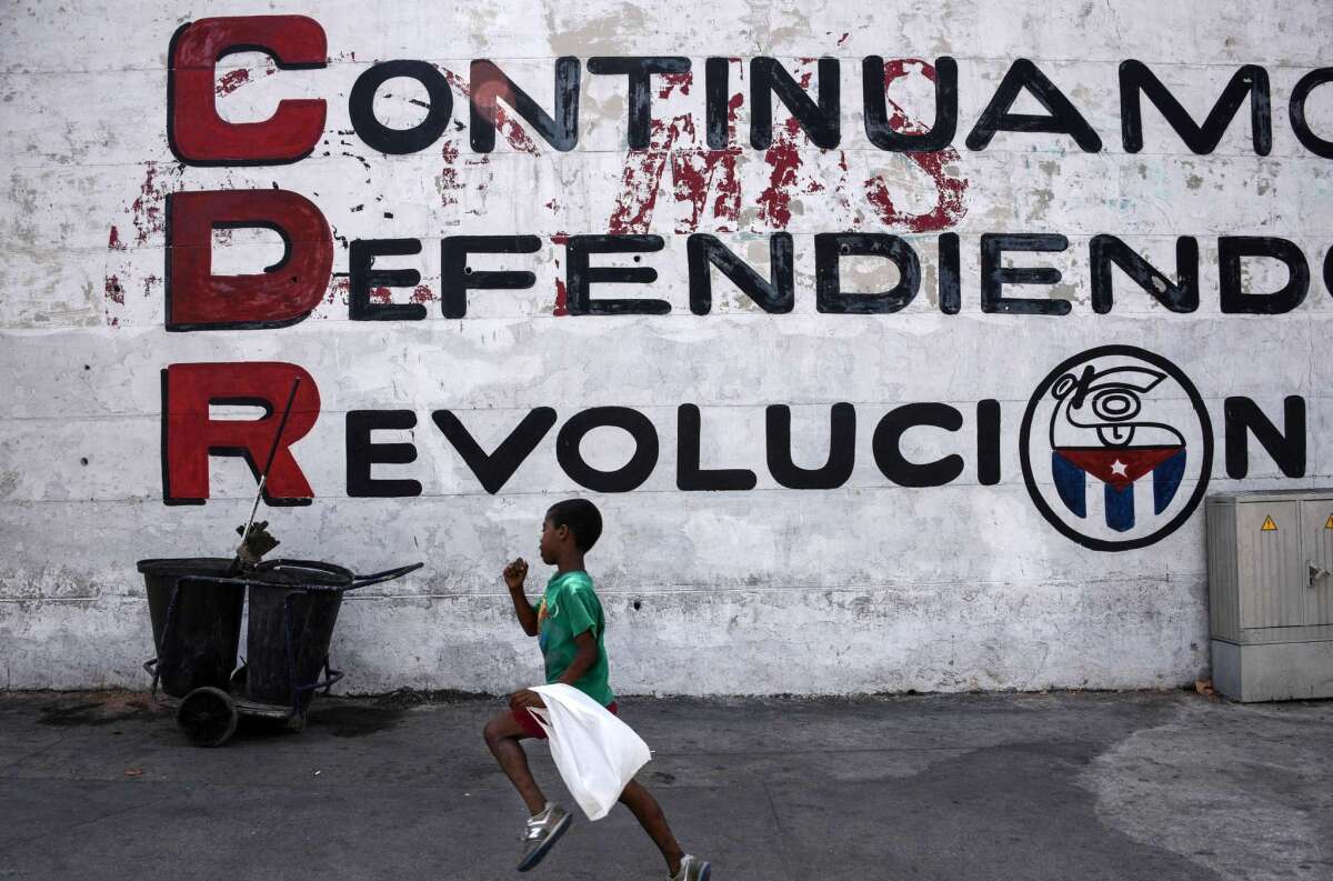 In Havana on the eve of President Obama's visit, a child runs in front of a wall reading "We keep defending the revolution."