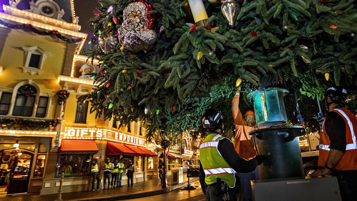 Workers use a crane to hoist the lower section of a giant Christmas tree into place as others decorate Disneyland's Main Street U.S.A.