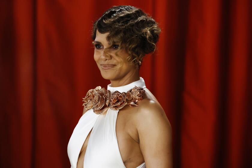 Halle Berry with a short haircut posing in a white gown with a golden flower collar