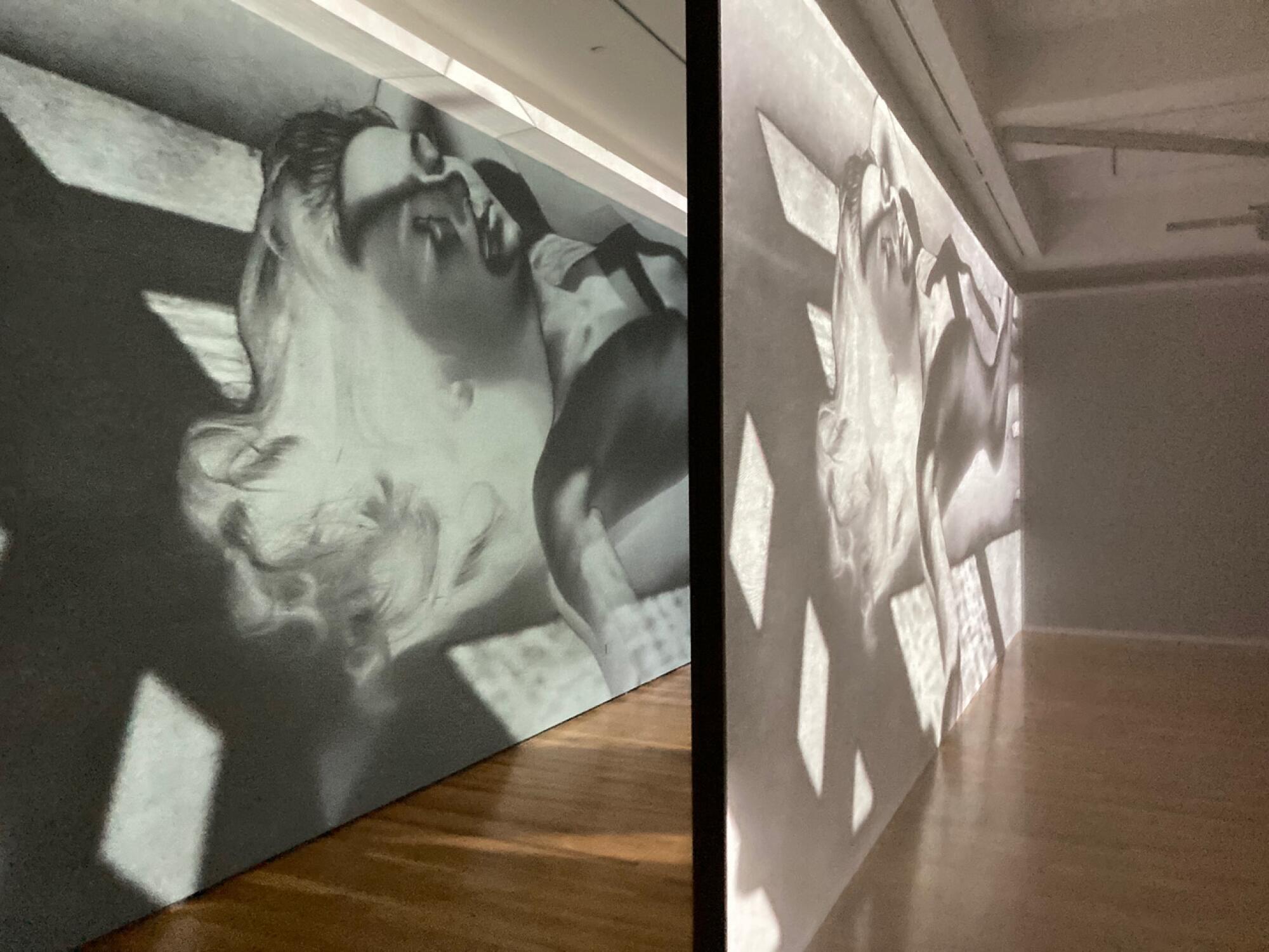 A pair of screens show a digital projection of a negative image of a beautiful woman lying on the ground.