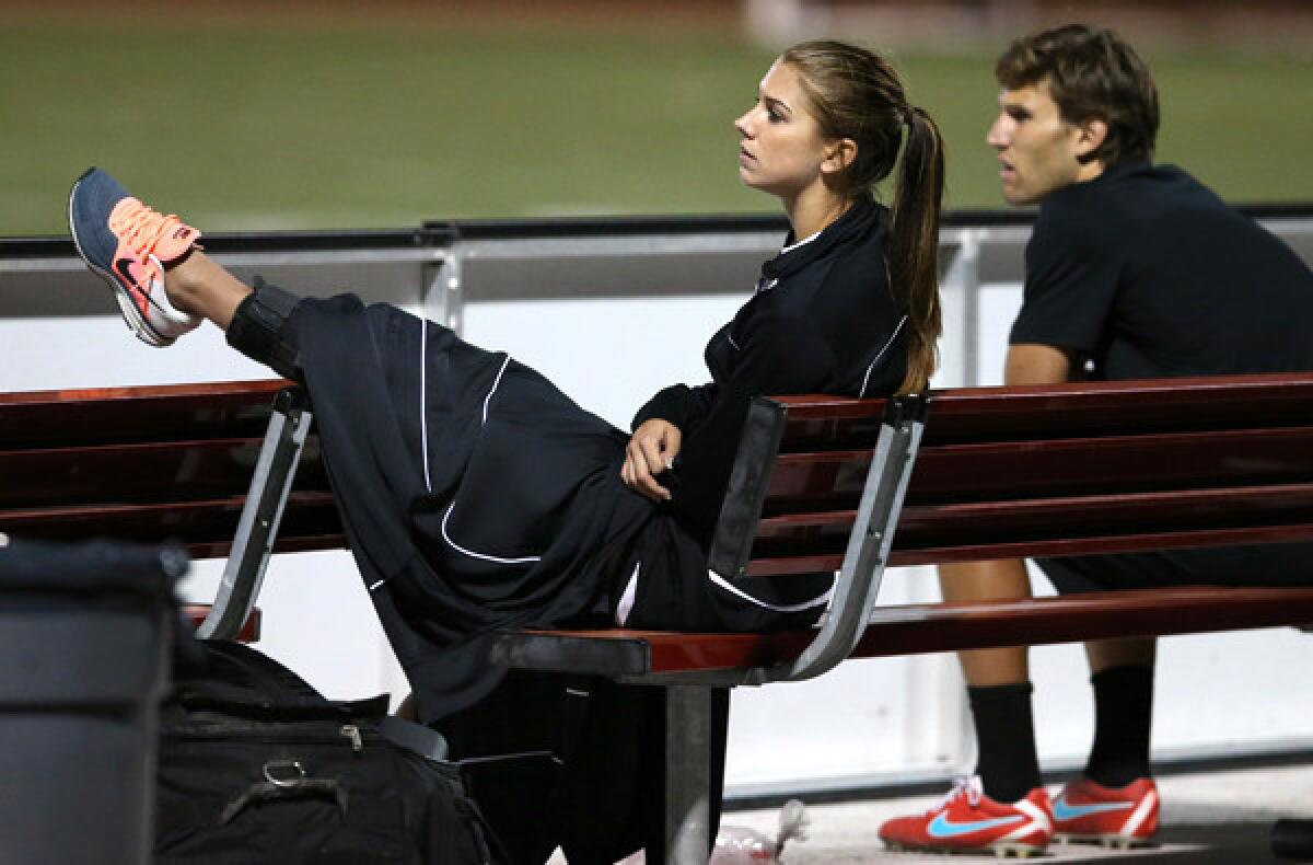 Portland Thorns forward Alex Morgan has her left leg propped up as she watches from the bench with fitness coach Nate Berry after injuring her knee in the first half of a NWSL game against the Breakers in Boston on Wednesday night.