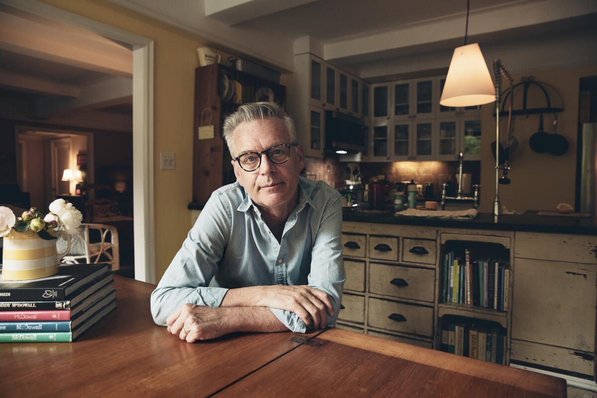 Michael Ritchie smiles while sitting at a wooden table in a room featuring wooden cabinets and books
