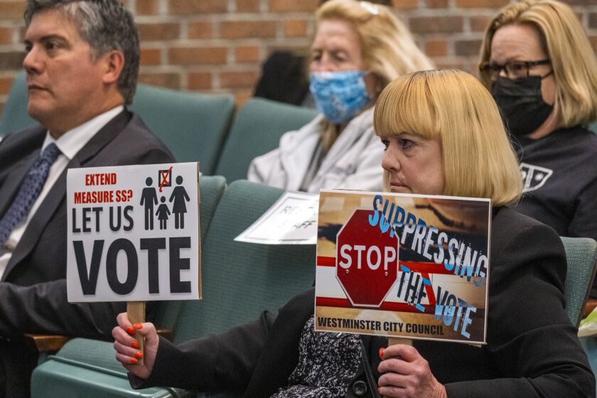 WESTMINSTER, CA - APRIL 13: Terry Rains holds up signs during a rare in-person City Council meeting during the pandemic on Wednesday, April 13, 2022 in Westminster, CA. The city of Westminster is facing bankruptcy. Instead of approving an extension of a sales tax measure that has helped to offset a $16 million budget deficit for the city, the council continues to argue over Vietnamese YouTube broadcasts spreading "fake news." (Francine Orr / Los Angeles Times)