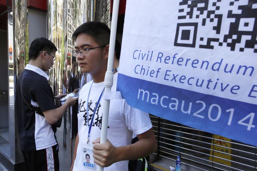 A man, left, uses a computer tablet to vote in an unofficial referendum in Macao, a semi-autonomous Chinese territory, as a volunteer helps hold a banner promoting the informal poll.