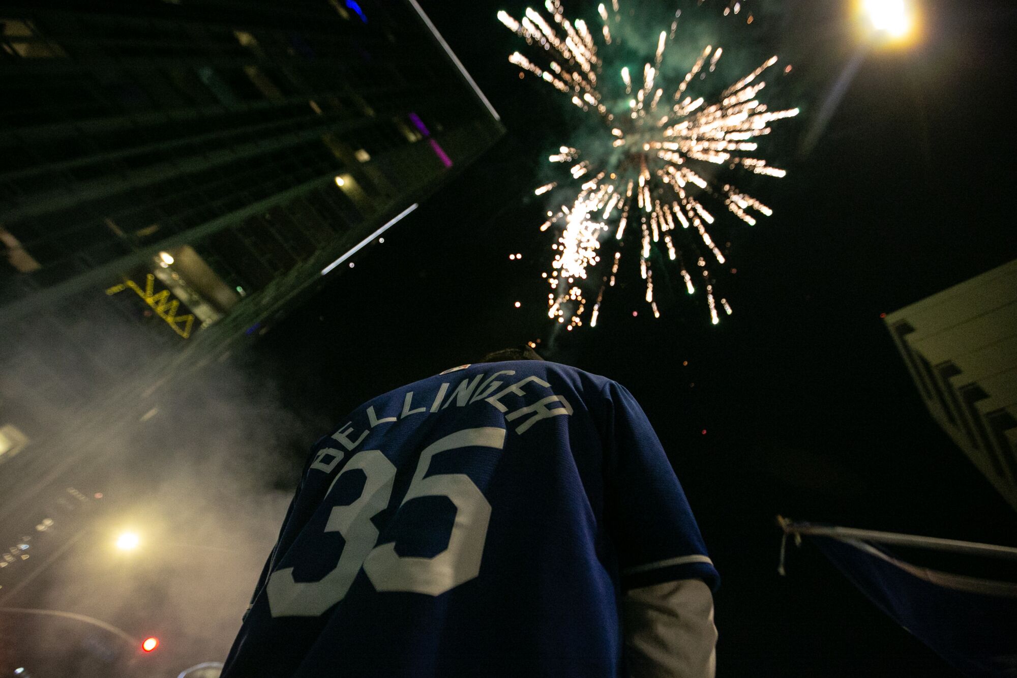 A person in a Cody Bellinger jersey is seen with fireworks exploding in the sky overhead.