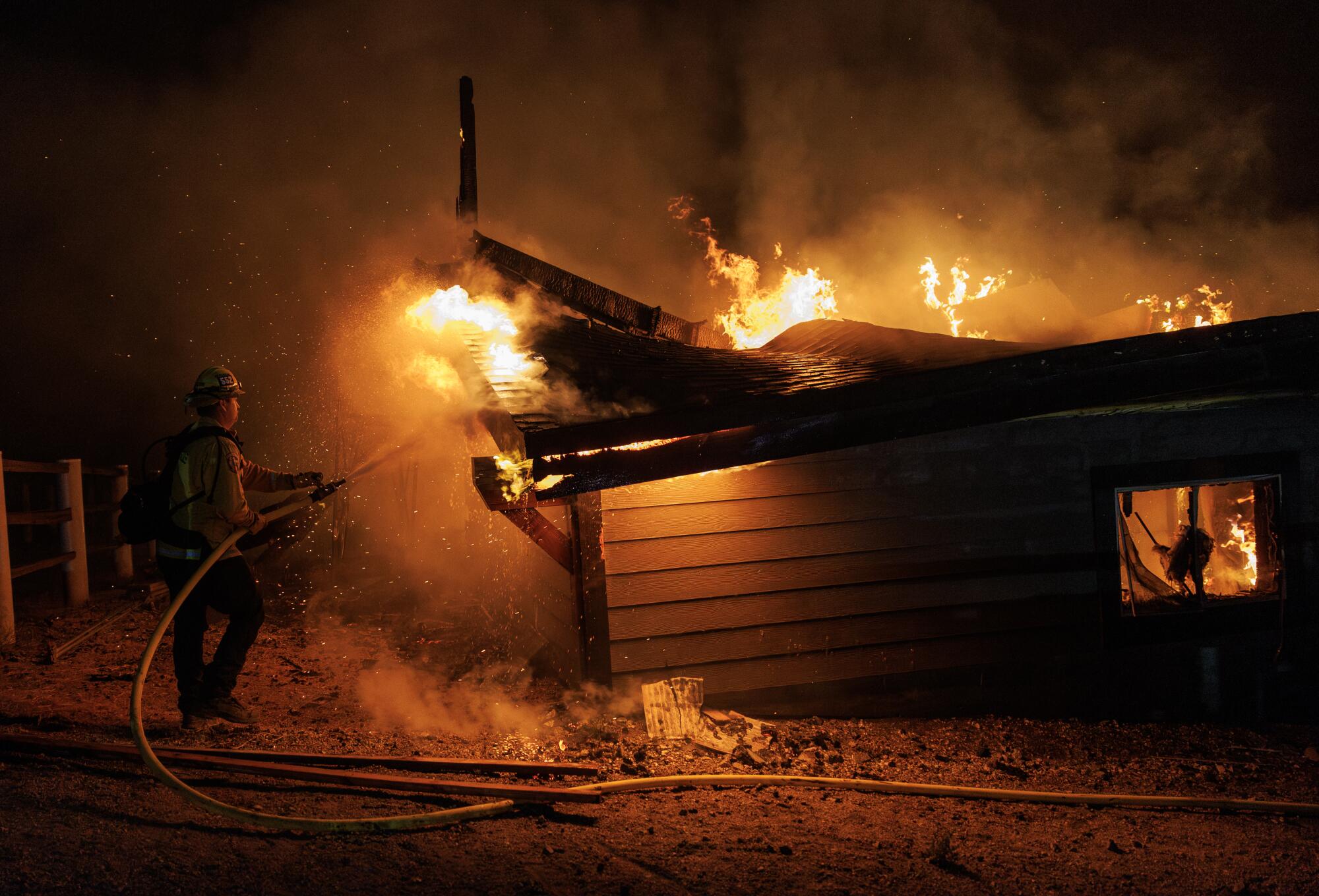 A firefighter sprays a burning barn.