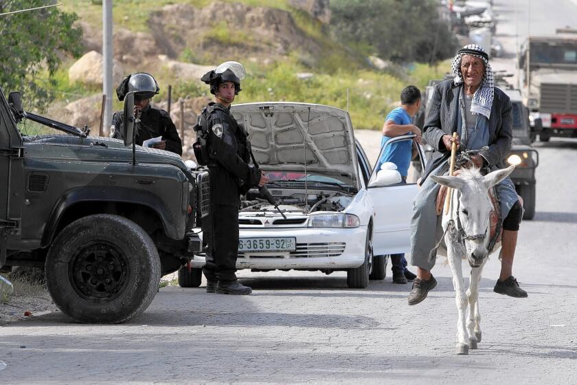 A Palestinian man rides a donkey past Israeli security officers conducting house raids in the West Bank village of Deir Sammit, in the wake of the fatal shooting of a police officer last week.