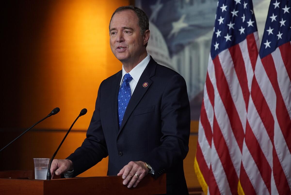 Representative Adam B. Schiff  stands at a lectern in front of U.S. flags