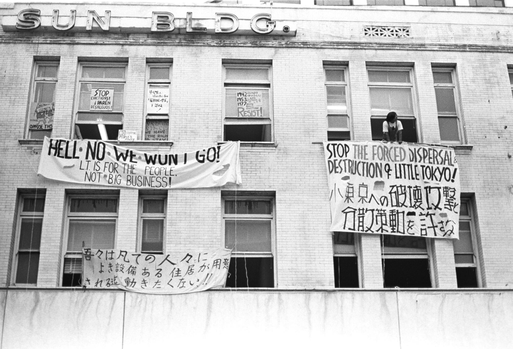 People hang protest signs outside the windows of a building.