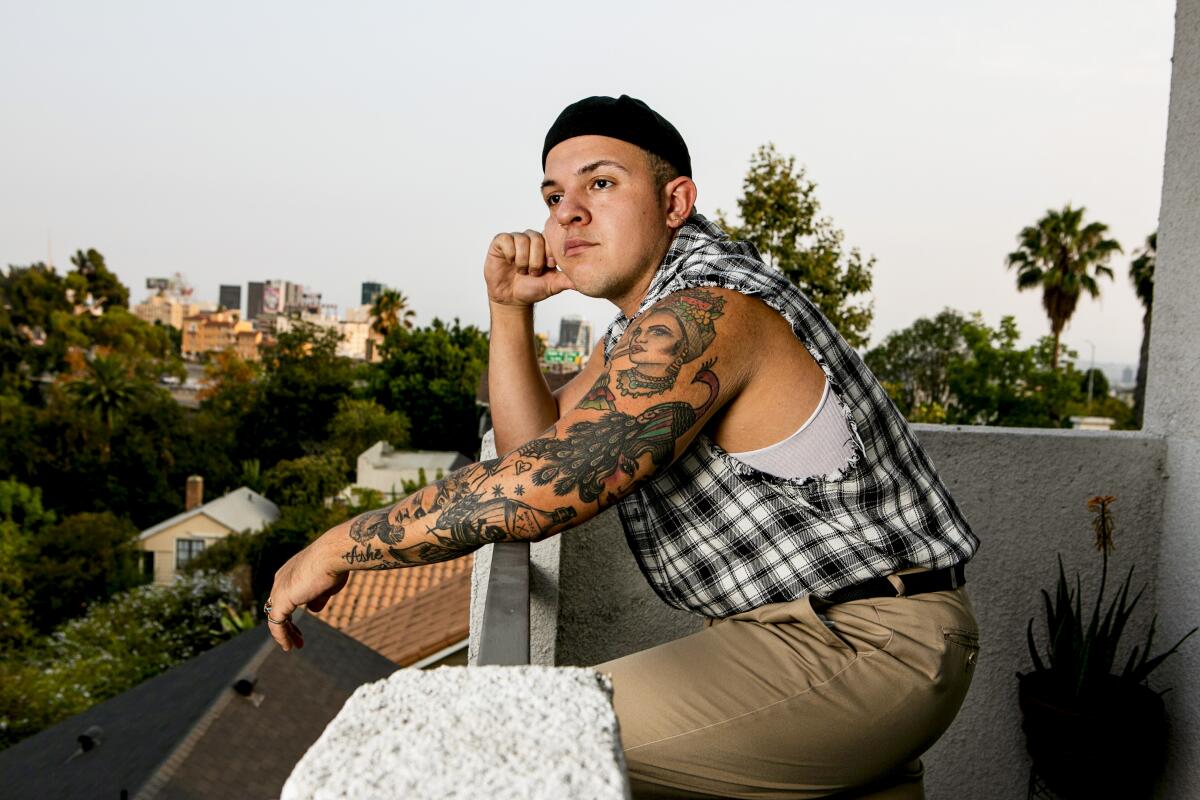 A man with an artfully tattooed arm stands on a balcony. 