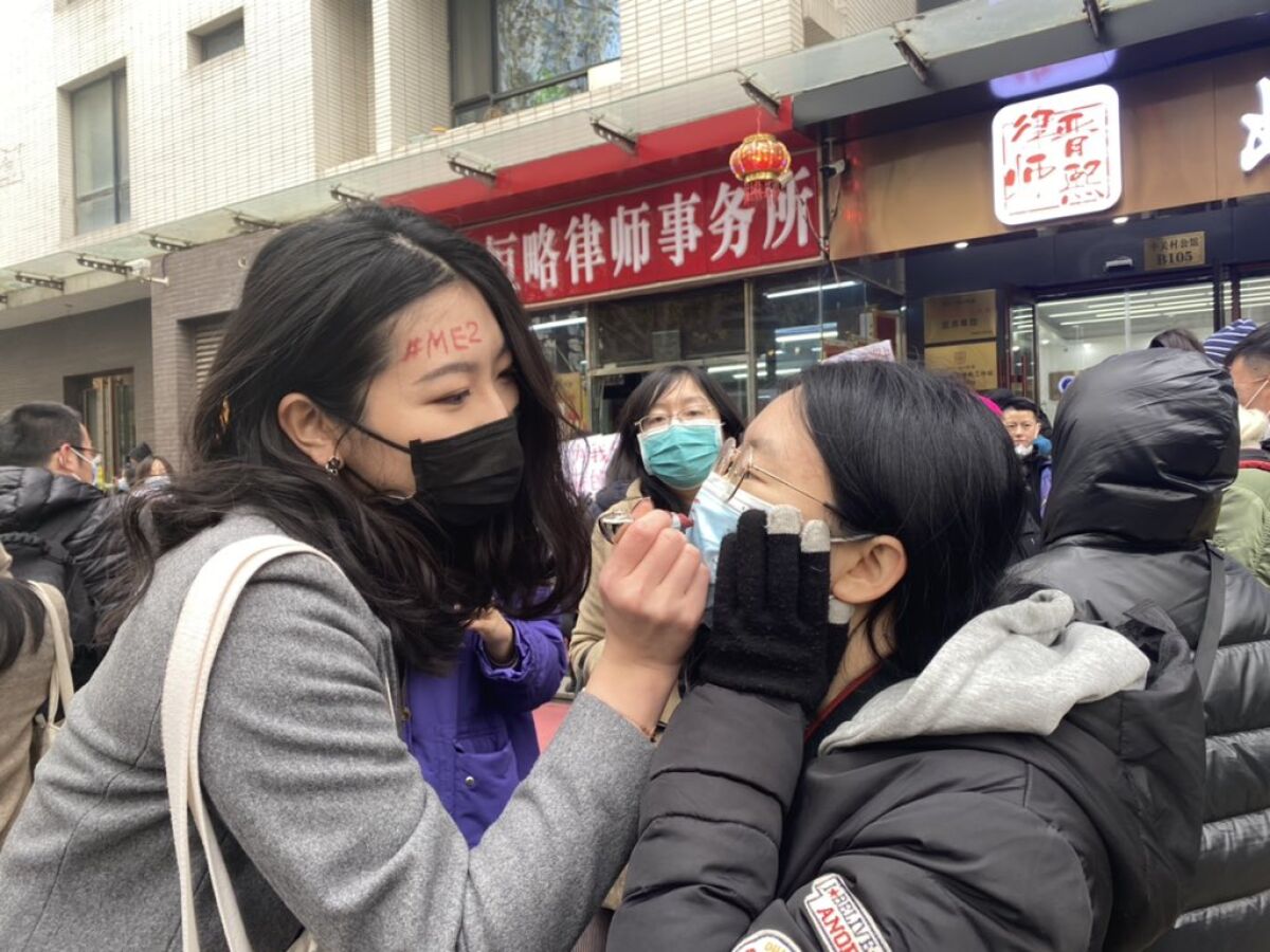 A supporter of Zhou Xiaoxuan uses lipstick to write #MeToo on a fellow supporter's mask in Beijing.