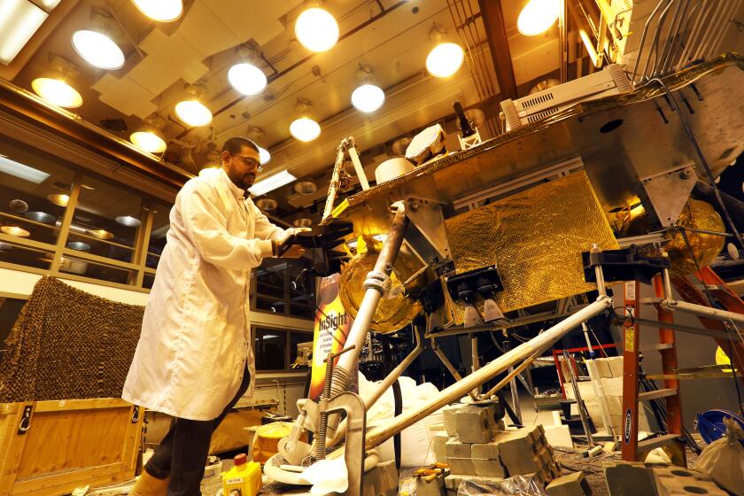 Pasadena, California -Dec. 7, 2022-Pranay Mishra, a systems engineer for NASA's Jet Propulsion Laboratory, next to InSight, a model of NASA's Mars InSight satellite. NASA's Mars InSight mission will likely end in January when dust covers the lander's solar panels and it stops transmitting data. ForeSight (a replica of InSight) has been put through all kinds of trials at JPL, and engineers are packing it up next week and putting it in storage now that the mission is expected to end. (Carolyn Cole / Los Angeles Times)