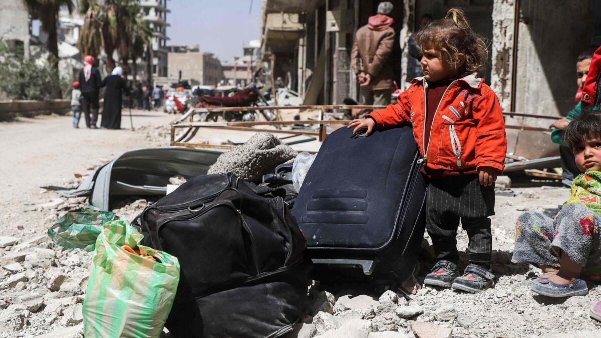 A Syrian child stands next to luggage with other civilians as they wait to be evacuated from the town of Arbin in the eastern Ghouta region on the outskirts of the capital Damascus.