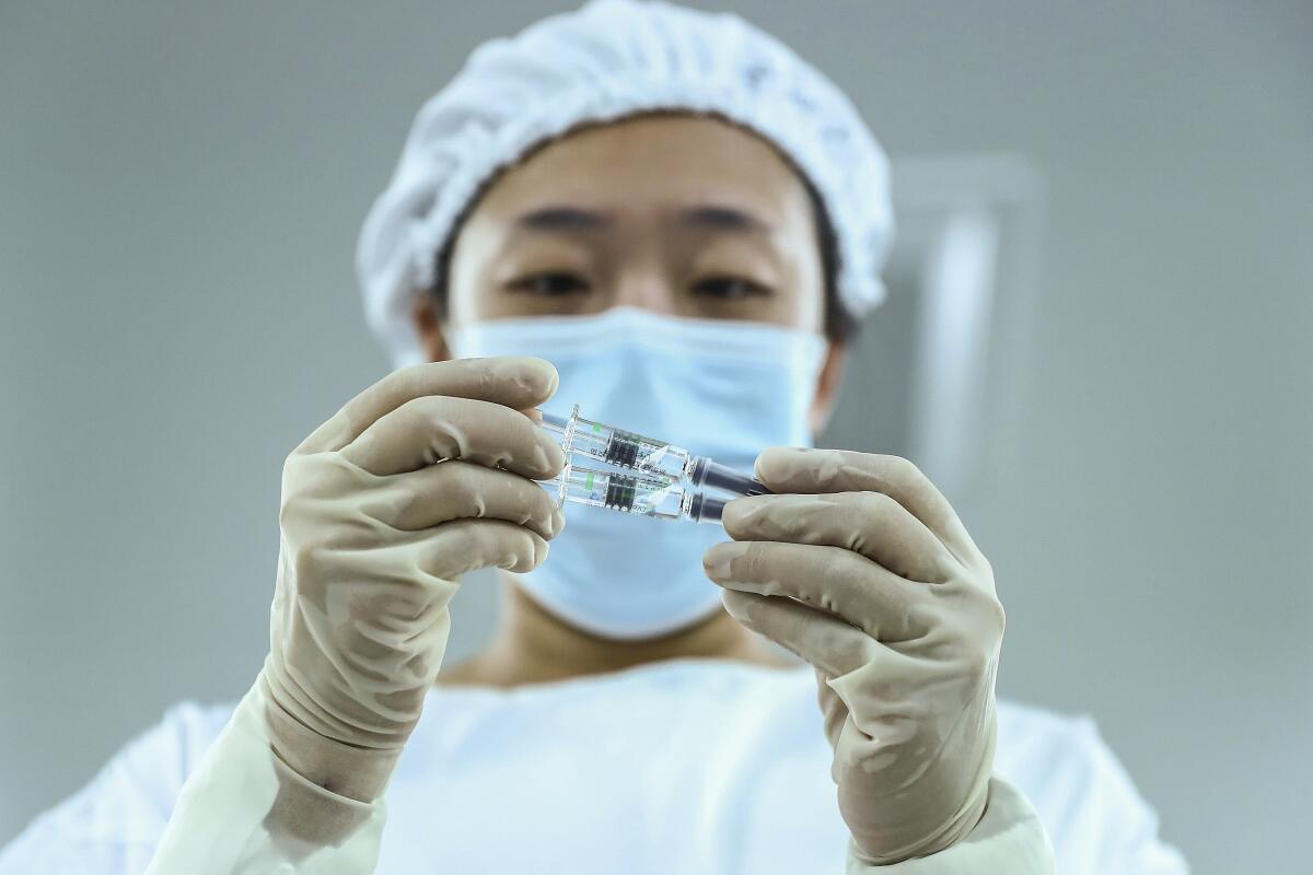 A worker holds up two syringes of vaccine to inspect