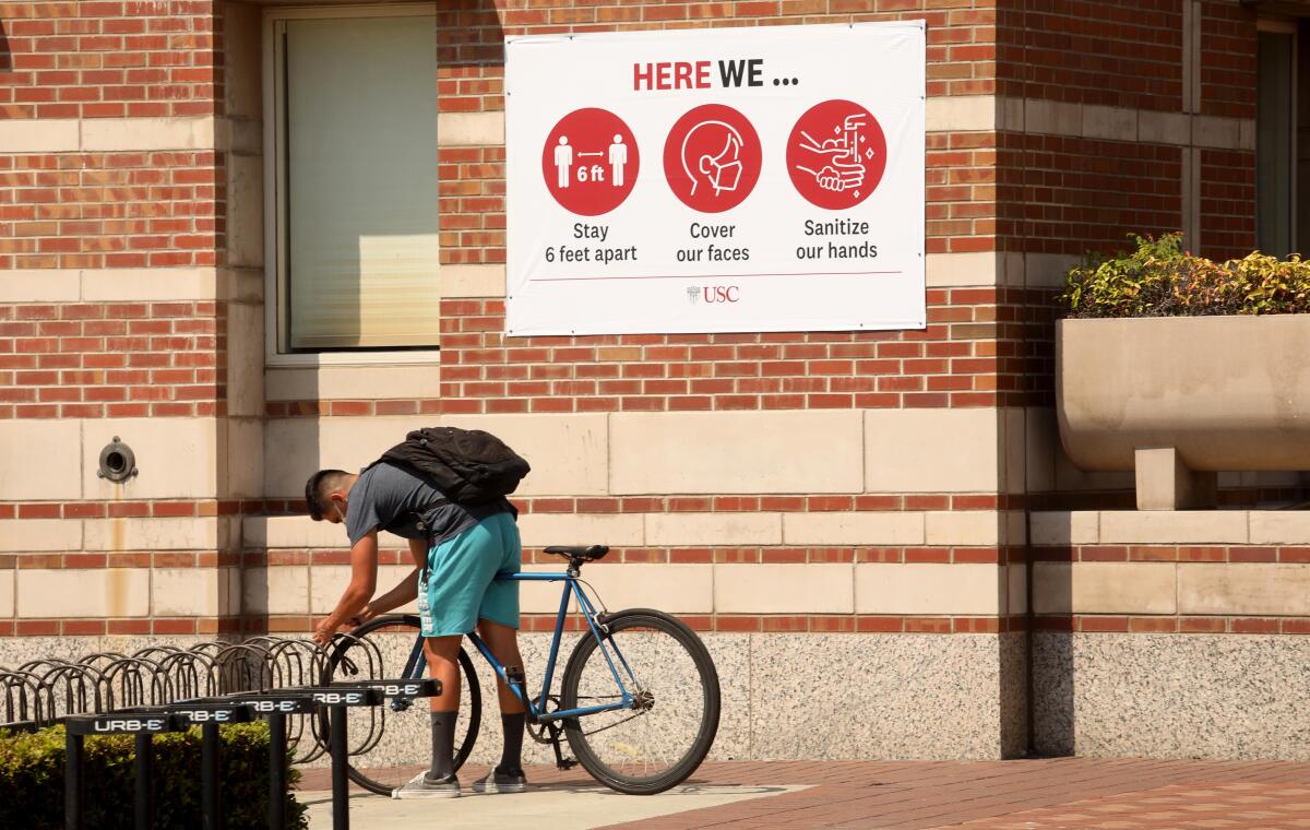 A USC student locks up his bike on campus under a sign that states three steps to keep the coronavirus at bay on Aug. 17.