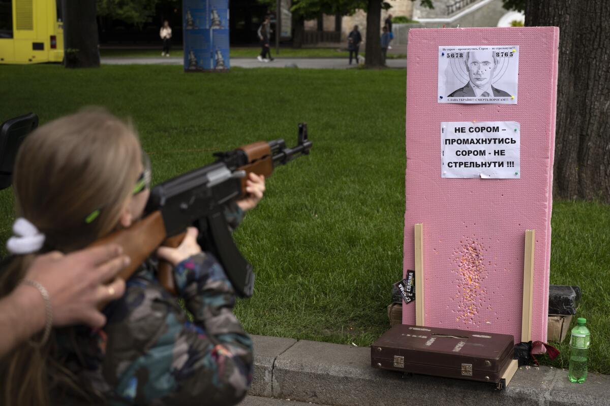 Ukrainian girl aiming plastic rifle at portrait of Russian President Vladimir Putin