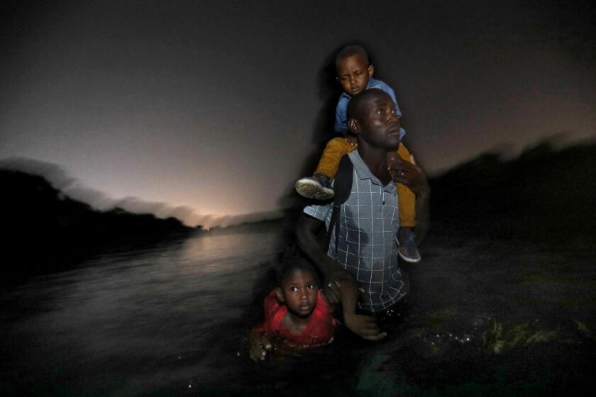 A Haitian man, with two children in two, wades across the Rio Grande to Del Rio, Texas.