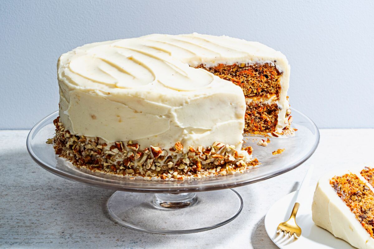 A layered carrot cake topped with cream cheese frosting is seen on a cake stand.
