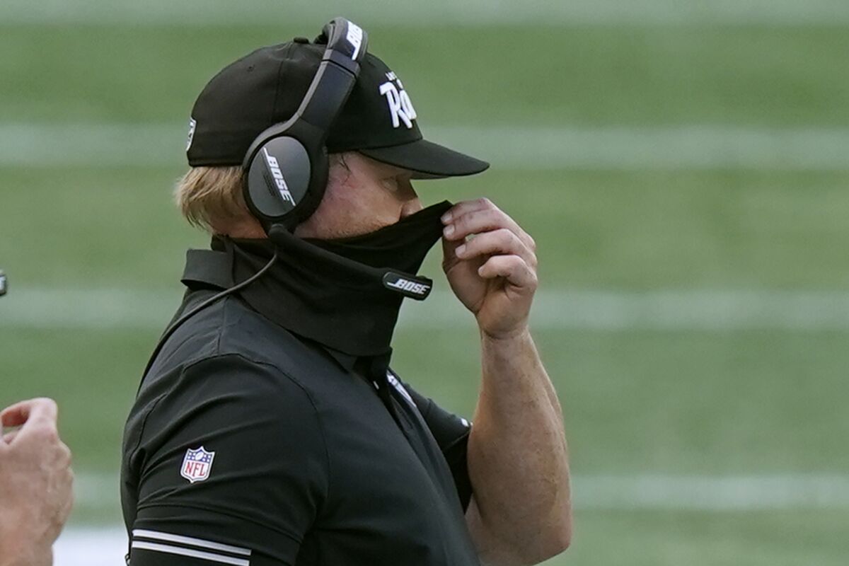 Las Vegas Raiders head coach Jon Gruden adjusts his protective face covering along the sideline.