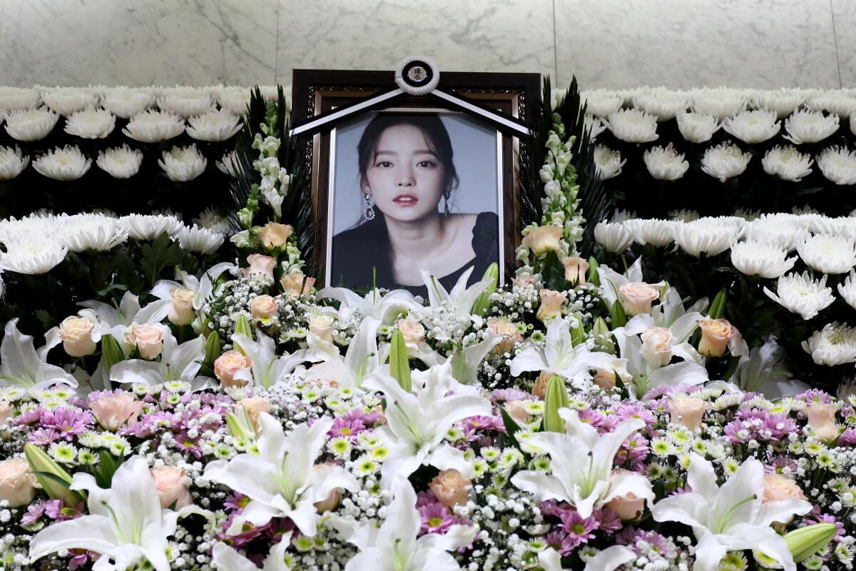 A memorial altar, surrounded by flowers, with a framed photo of K-pop star Goo Hara.