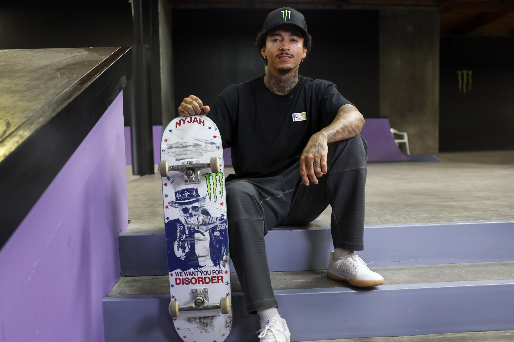 Skateboarder Nyjah Huston sits while holding his skateboard.