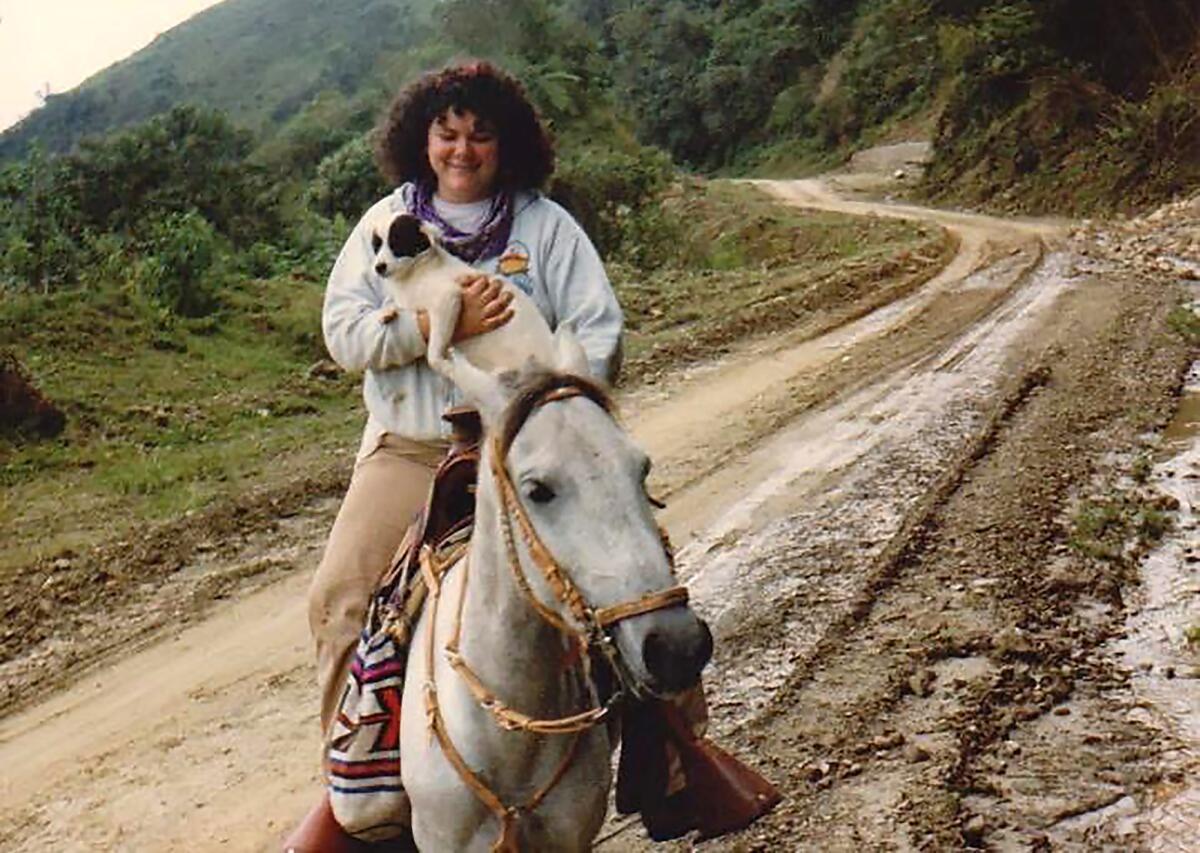 A woman on horseback holds a small dog.